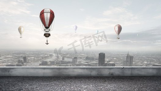 浮气球摄影照片_在城市上空飞行的空气调节器。五颜六色的浮空器在现代城市上空的晴空中飞舞