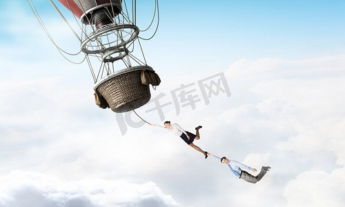 浮空器摄影照片_女人和男人在浮空器上飞行。年轻的女商人和男人骑着五颜六色的浮空器在天空中高高飞行