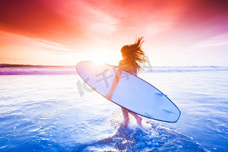 冲浪女孩摄影照片_日落时海滩上的冲浪女孩。夕阳西下海滩上美丽性感的冲浪女孩