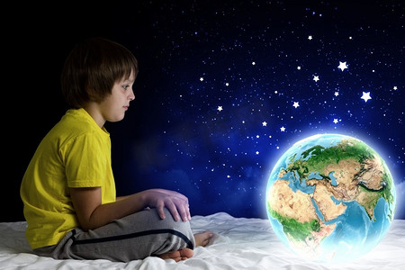 可爱元素摄影照片_晚上做梦。可爱的男孩坐在床上举行地球行星。这张图片的元素是由美国宇航局提供的