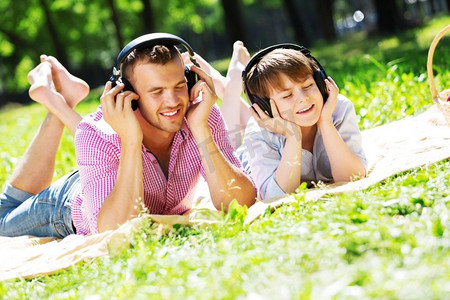 自然旋律摄影照片_父亲和孩子在夏天公园享受音乐。周末在公园