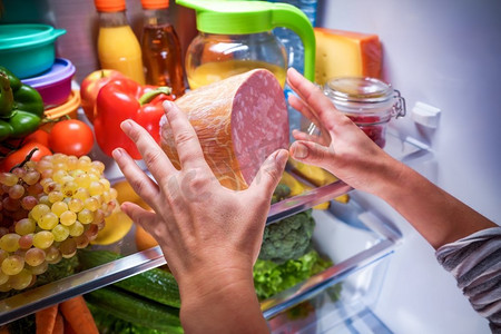在敞开的冰箱里，人的手在晚上伸手拿食物
