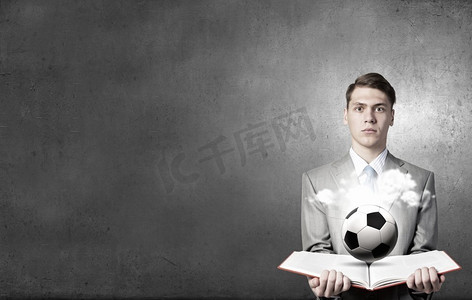 打开书本的男人。年轻的商人手里拿着书，书页上放着足球