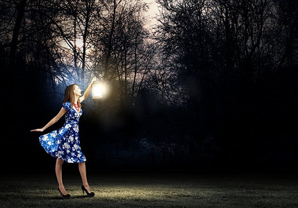 蓝色元宵灯笼摄影照片_带灯笼的女人。年轻女子在蓝色的衣服走在夜间木材