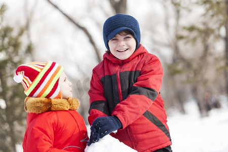 可爱的男孩和女孩在冬季公园堆雪人。冬季活动小游戏