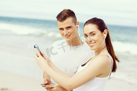 户外有移动智能手机的跑步者夫妇。有移动智能电话的赛跑者的年轻夫妇户外在海滩