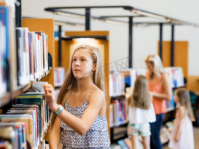 十几岁的女孩挑选一本书在公共图书馆。这是一个艰难的选择