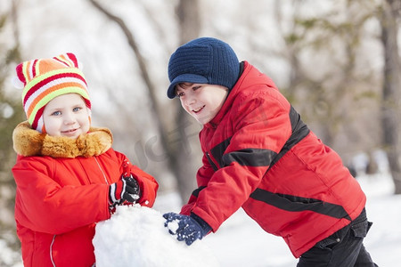 小游戏冲鸭摄影照片_可爱的男孩和女孩在冬季公园堆雪人。冬季活动小游戏