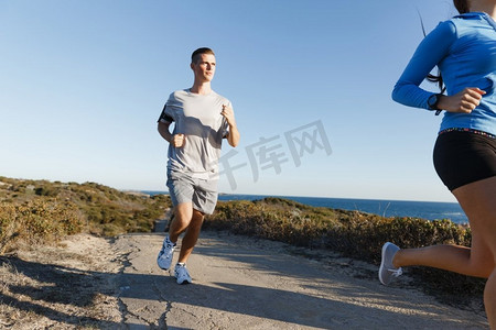 运动跑步者在海滩上慢跑，和她的伴侣一起锻炼。健康的女健身模特和她的伴侣沿着海洋慢跑