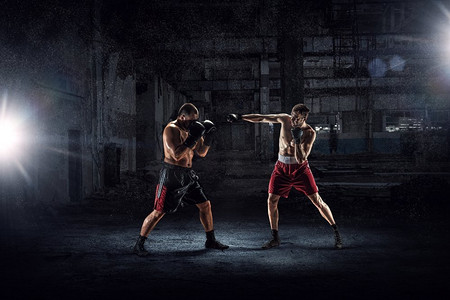 中的战斗机摄影照片_两个拳击手的战斗。强大的拳击手在黑暗的工业内部混合媒体中战斗