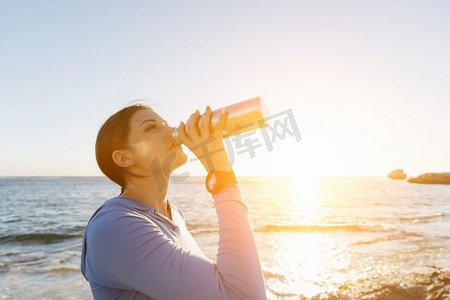 女人在海滩上喝水。年轻女子饮用水后行使在海滩上