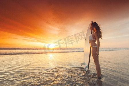 日落时海滩上的冲浪女孩。夕阳西下海滩上美丽性感的冲浪女孩