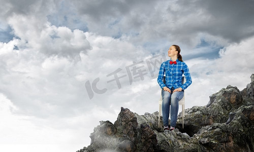 坐在椅子摄影照片_隔离的概念。一位穿着休闲服装的年轻女子坐在岩石上