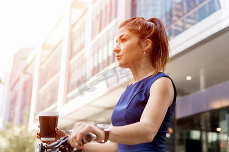 骑自行车上下班的年轻女子。穿着公务服的年轻女子骑着自行车喝着咖啡