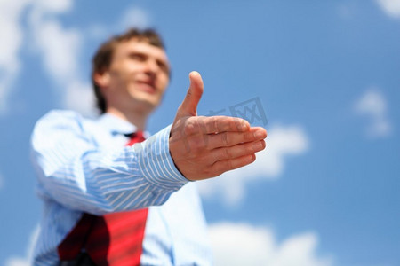伸出手摄影照片_一位穿着蓝色衬衫，打着红色领带的年轻商人伸出手握手