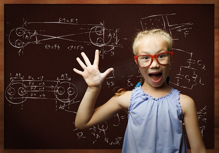 黑板公式摄影照片_聪明的女学生。戴着红眼镜的天才女孩在黑板上写着公式