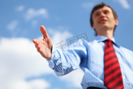 伸出手摄影照片_一位穿着蓝色衬衫，打着红色领带的年轻商人伸出手握手