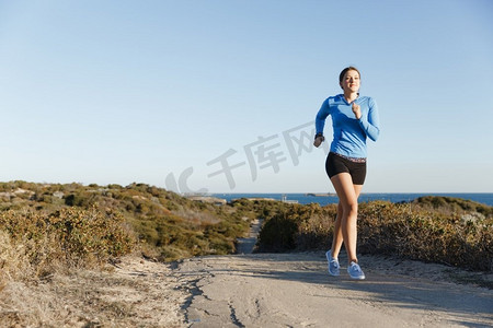 模特跑步摄影照片_运动跑步者在海滩上慢跑锻炼。健康的女性健身模特沿着海洋慢跑