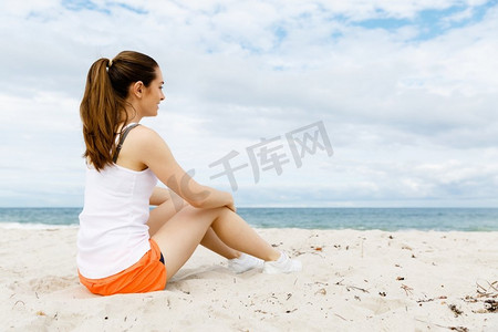 一分钟摄影照片_一位穿着运动服的年轻女子坐在海滩上。穿着运动服的年轻女子独自坐在海滩上休息一分钟
