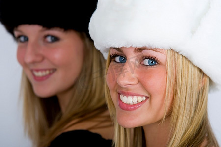 两个戴着毛皮帽的美丽的俄罗斯女人，以四分之三的侧写拍摄，一个对焦，一个出来，但都对着相机微笑
