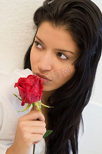 工作室拍摄的一幅美丽得令人惊叹的西班牙女孩闻着红玫瑰的肖像