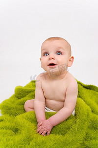 一个蓝眼睛的婴儿聚精会神地坐在毛茸茸的绿色毯子上
