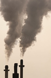 工业烟囱摄影照片_在金色的傍晚光线下，烟囱冒出污染。