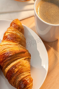 早餐牛角面包和一杯热咖啡，金色的清晨阳光照耀着