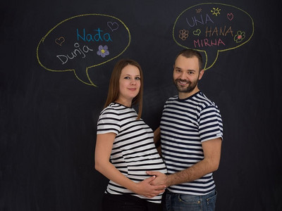 丈夫和怀孕的妻子在黑色粉笔画板前摆姿势的肖像。怀孕夫妇在黑色粉笔画板前摆姿势