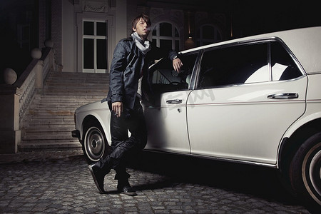 豪华车背景摄影照片_英俊的年轻人站在豪华轿车旁边