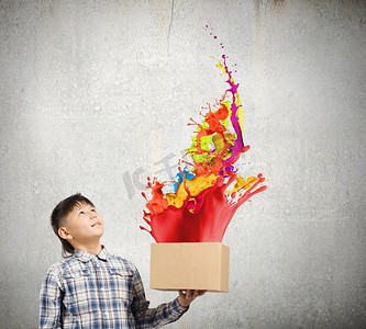 创意概念。可爱的男孩从纸盒上溅起五颜六色的油漆