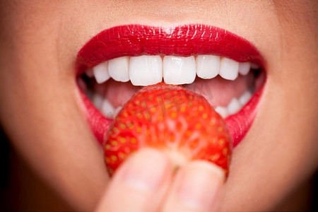 一张美丽的女性嘴巴吃着新鲜草莓的微距特写