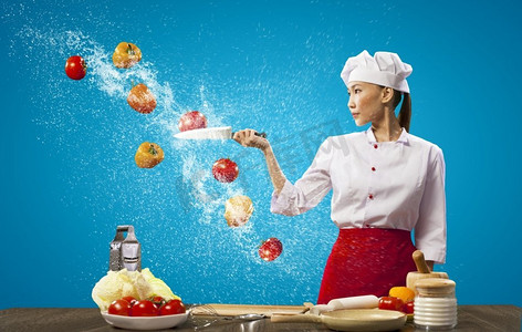 刀切水果摄影照片_亚裔女厨师用刀做饭。亚洲女厨师在空中用刀切水果和蔬菜