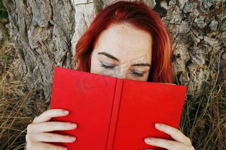 年轻女子读一本红色的书在秋天          