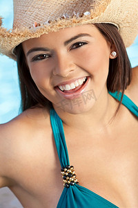 一位性感美丽的拉美裔年轻女子，穿着比基尼，戴着草帽，身后有个游泳池，笑着