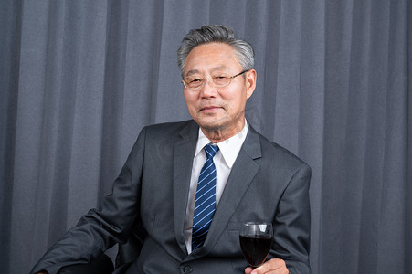  一个成功的商务老年人坐在老板椅上拿着红酒