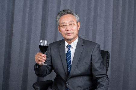&nbsp;一个成功的商务老年人坐在老板椅上拿着红酒