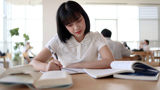 书写女孩摄影照片_图书馆看书的女大学生学习阅读书写作业