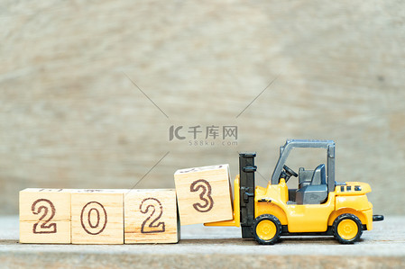 Toy forklift hold letter block 3 to complete word 2023 on wood background