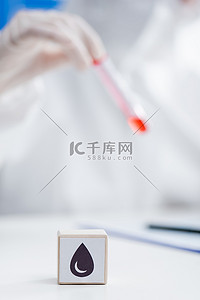 cropped view of blurred doctor holding test tube with blood sample near cube with drop icon, omicron variant concept