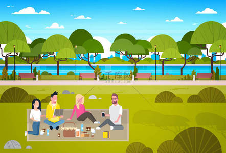 快乐的人有野餐在公园小组的年轻男子和妇女坐在草地上放松