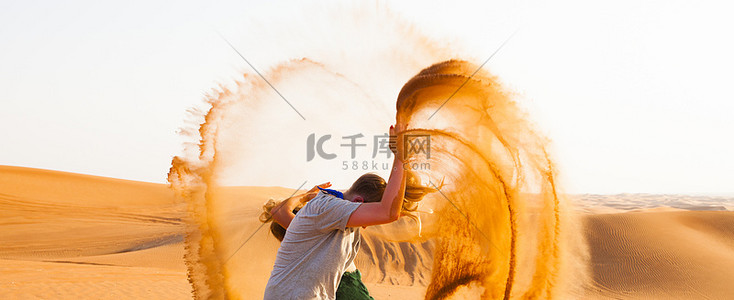女孩有乐趣与投掷沙漠沙子在空气中