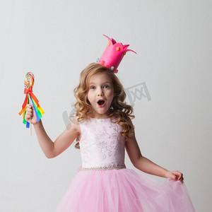美丽兴奋的糖果公主女孩在皇冠拿着大棒棒糖。糖果公主女孩在皇冠