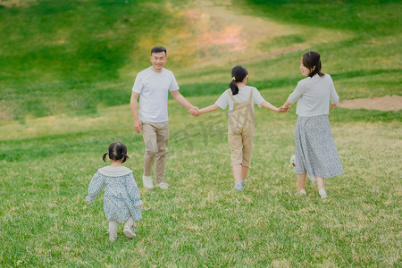 爸爸妈妈拉着孩子的手走在公园的草地上