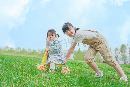 姐姐推着妹妹在草坪上玩耍