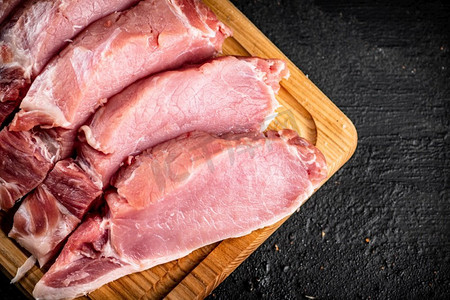 生猪肉切片在木砧板上。黑色背景。高质量的照片。生猪肉切片在木砧板上。 