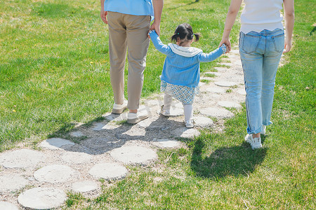 爸爸妈妈拉着小孩的手穿过绿草坪的铺石砖的小路