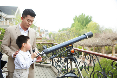儿童望远镜摄影照片_父亲和儿子在阳台使用天文望远镜