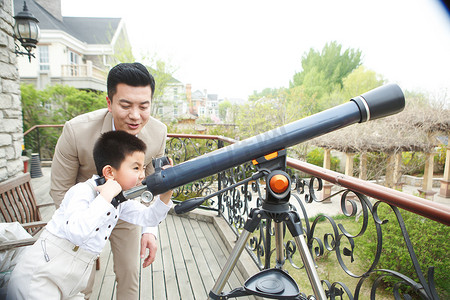 儿童望远镜摄影照片_父亲和儿子在阳台使用天文望远镜