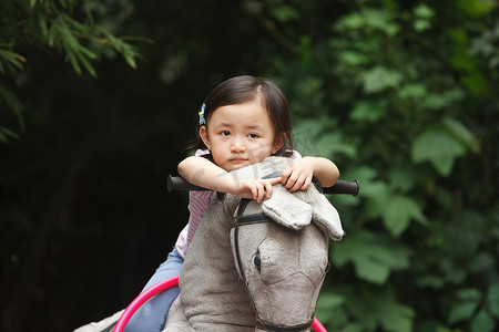 动物幼儿园摄影照片_可爱的小女孩在骑摇摆木马